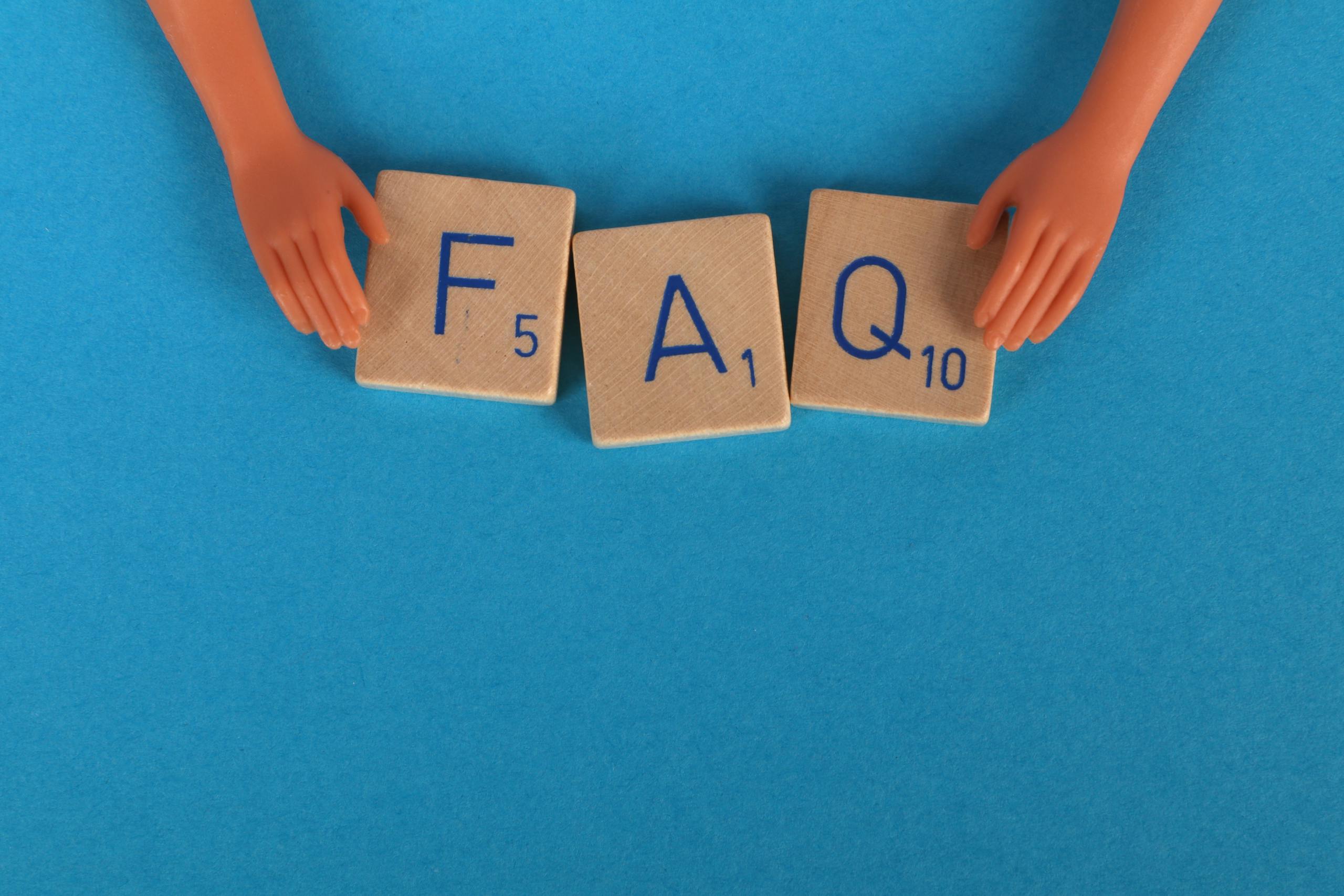 Flat lay of scrabble tiles spelling 'FAQ' with toy hands on a blue background, creating a conceptual image.