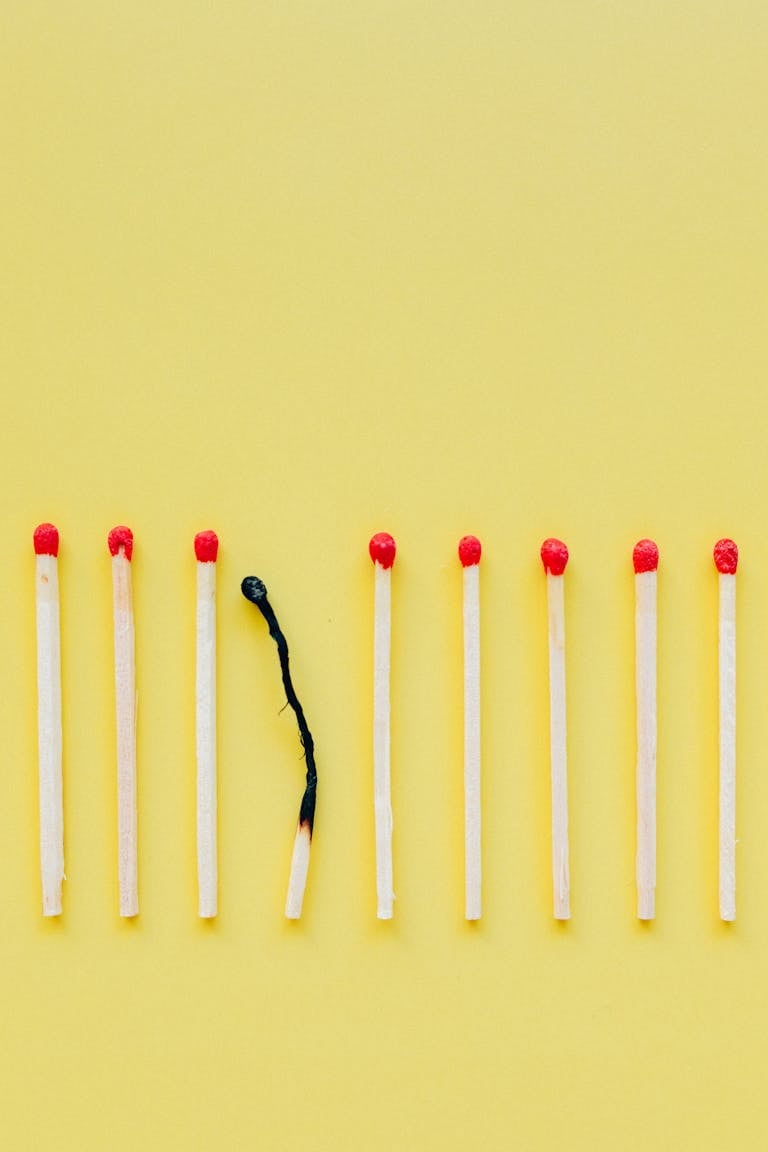 A line of matchsticks with one burned out against a yellow background.