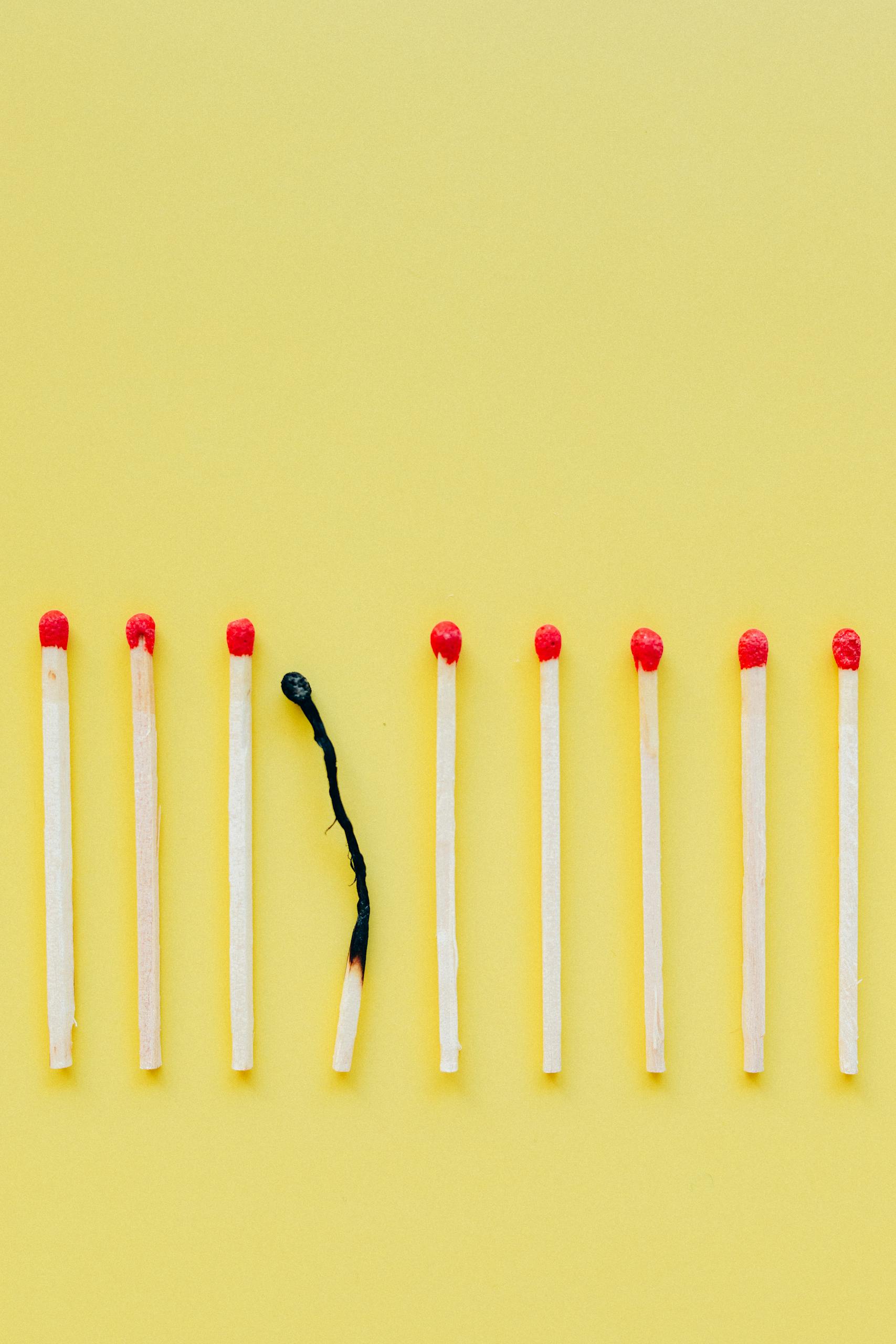 A line of matchsticks with one burned out against a yellow background.